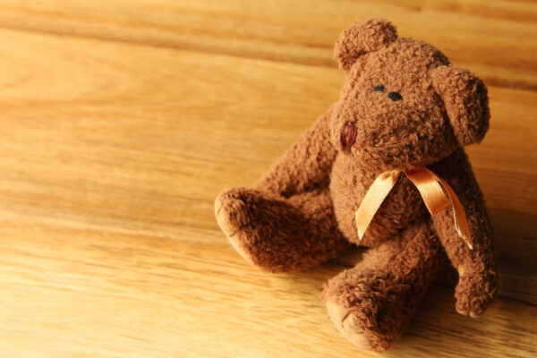 A small brown teddy bear sitting on a wooden floor. This image can be used to represent children's toys or child care.