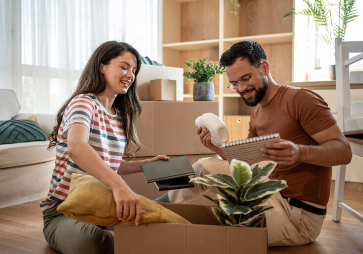 Happy couple unpacking boxes in new home after moving house Young couple smiling and unpacking boxes in their new home, embracing the excitement of starting a fresh chapter in life together after relocating to a new space